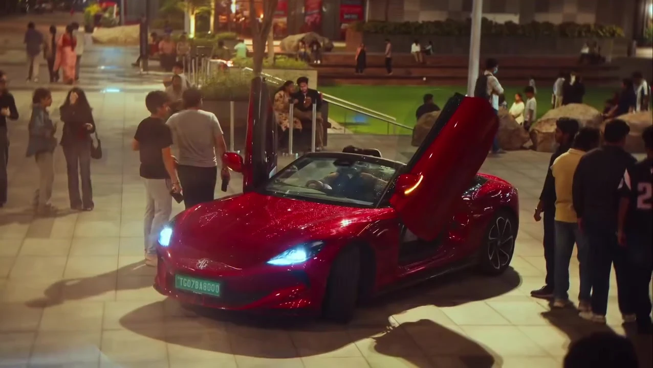 A red roadster with scissor doors open surrounded by onlookers at night